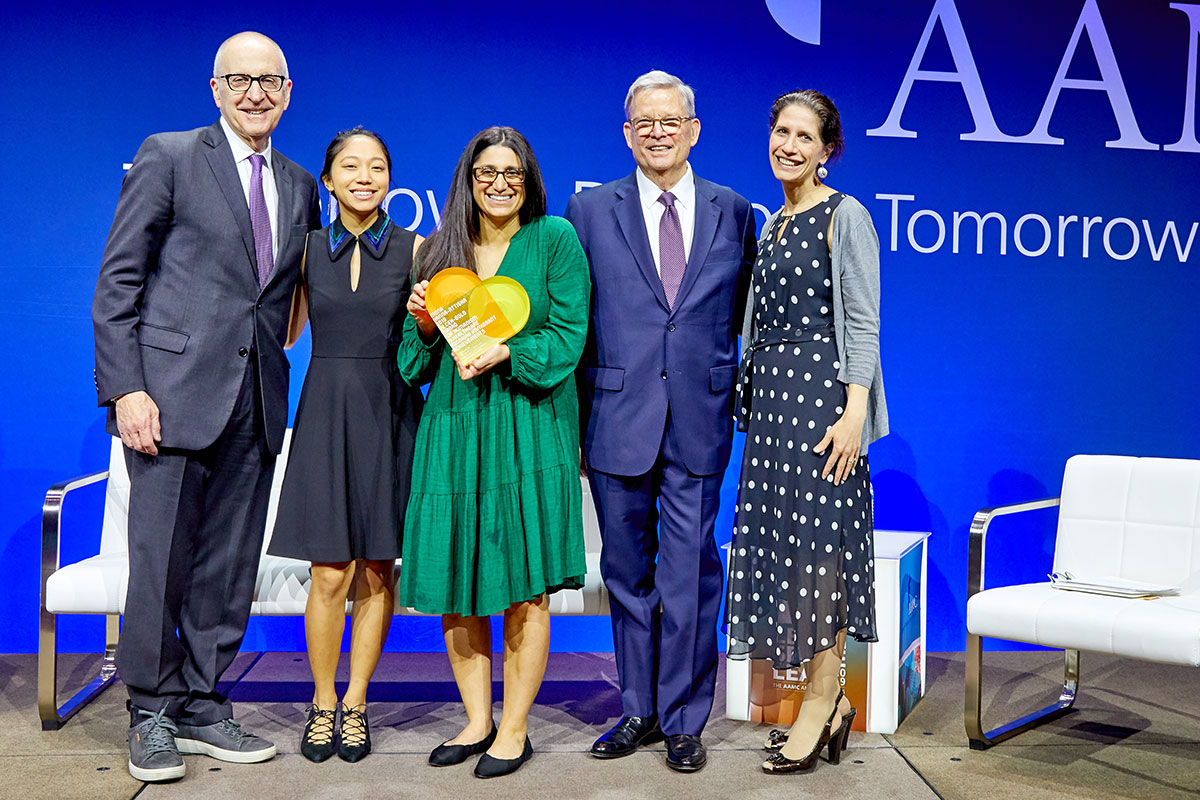 Mona Hanna-Attisha stands on stage, accepting an award, surrounded by two other people on each side.