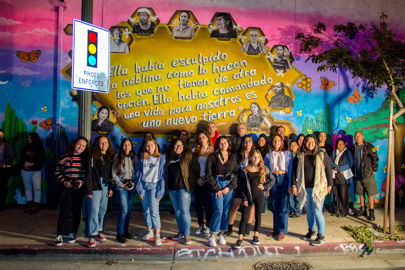 Students in front of Migrant Mamas mixed-media mural, featuring their portraits of inspirational migrant women