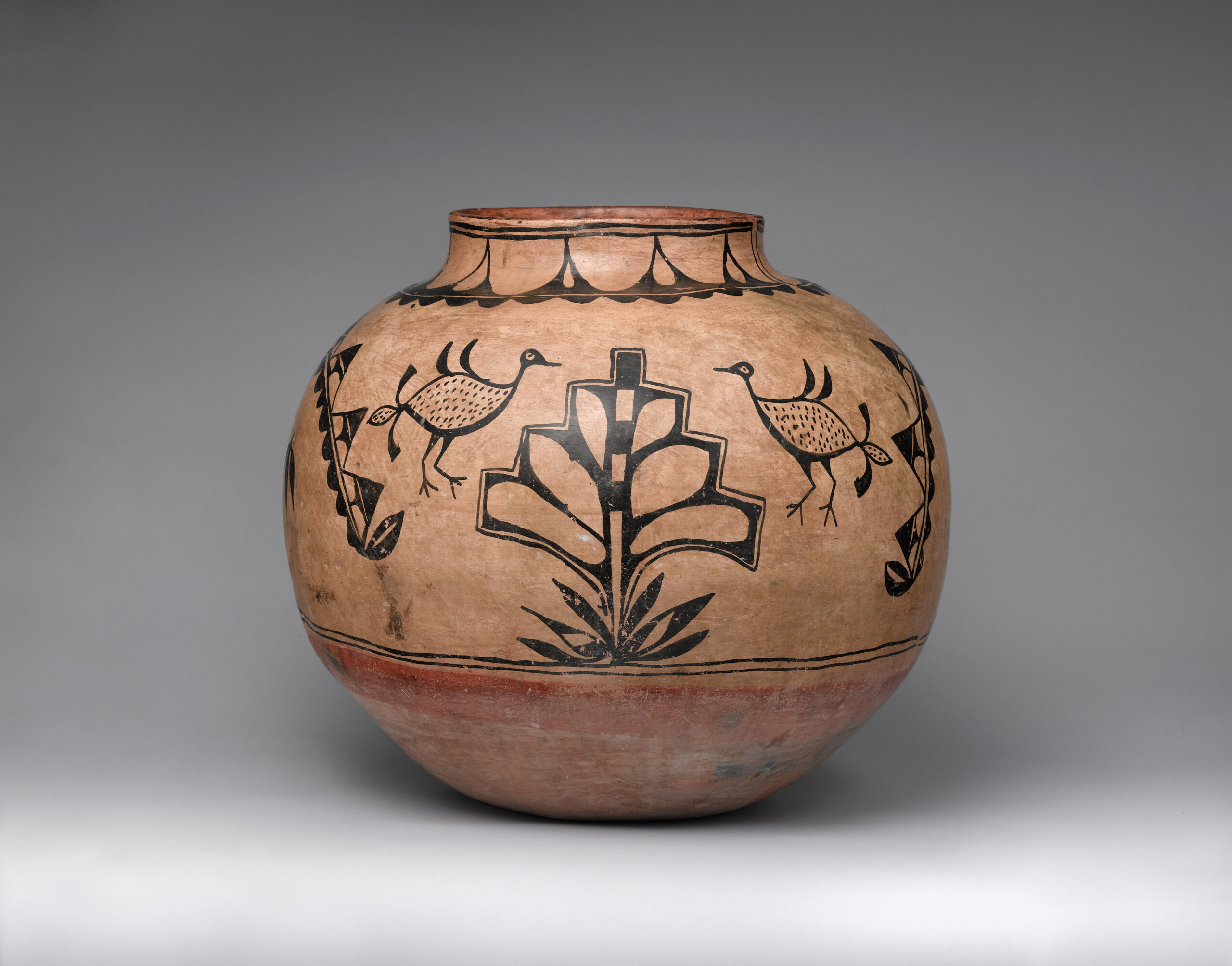 A brown Cochiti jar painted with a black design including leaves, a plant, and four birds.