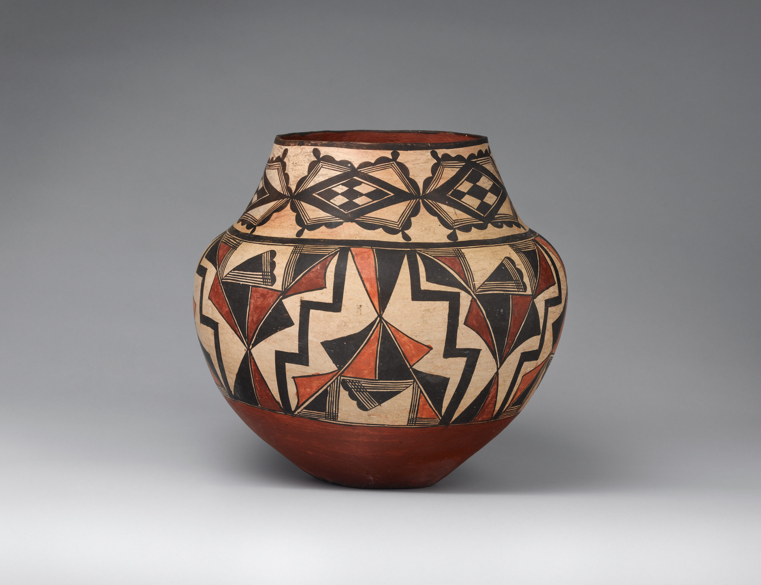 An Acoma jar decorated with black, beige, rust-brown, and red geometric patterns.
