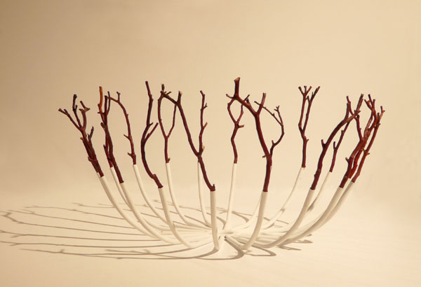 An off-white bowl made of steel prongs and dark red twigs.
