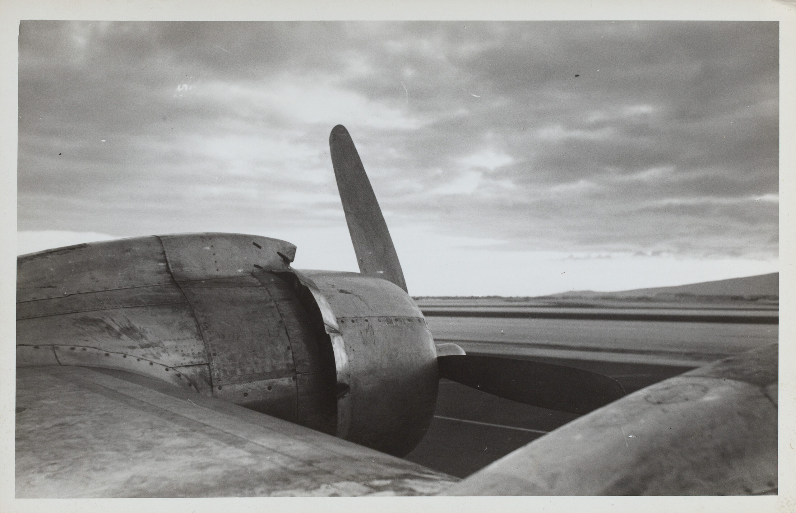 Black and white photograph of a plane propeller against a cloudy horizon.