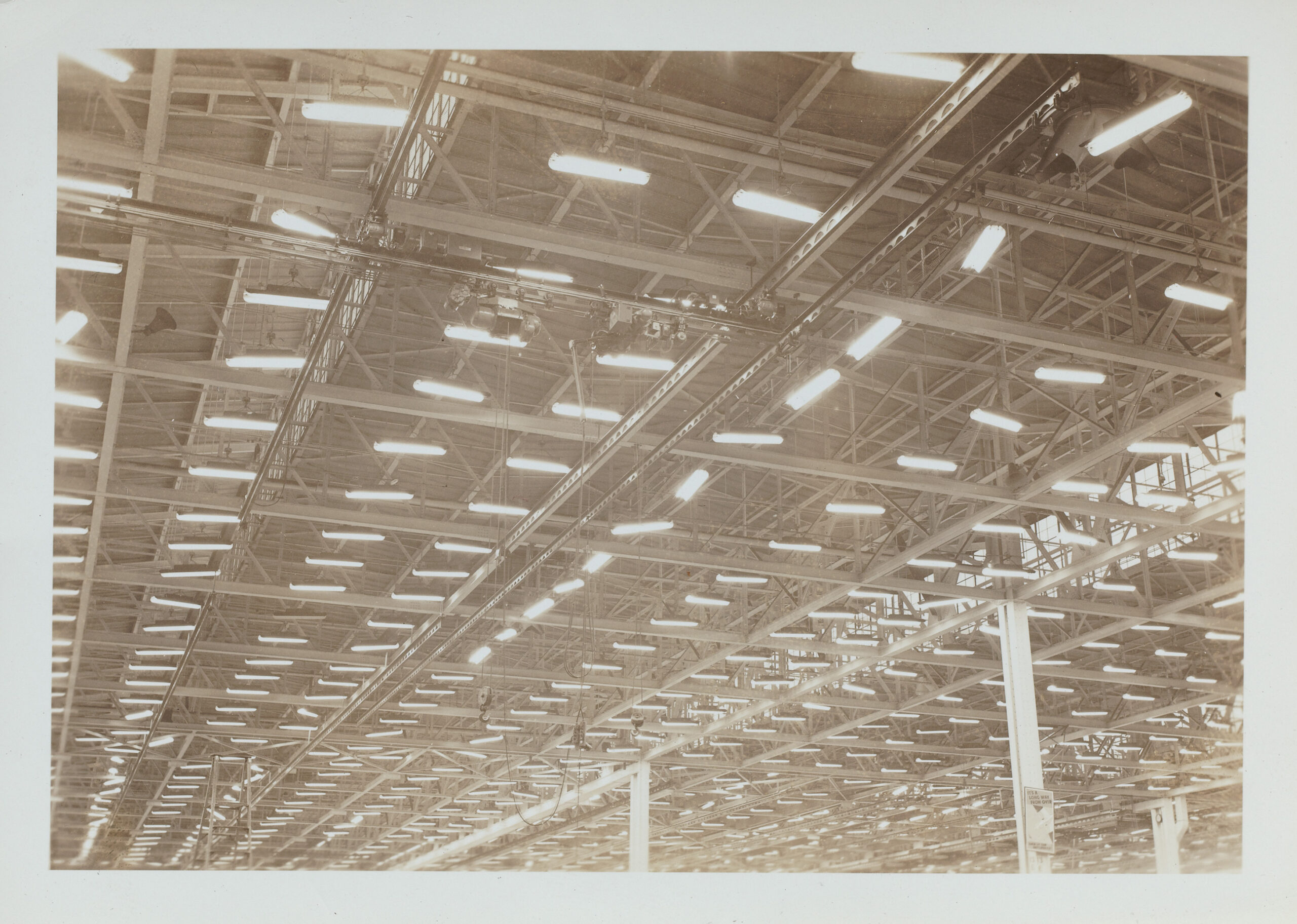 Black and white photograph of rows of light fixtures on the ceiling of an aircraft factory.