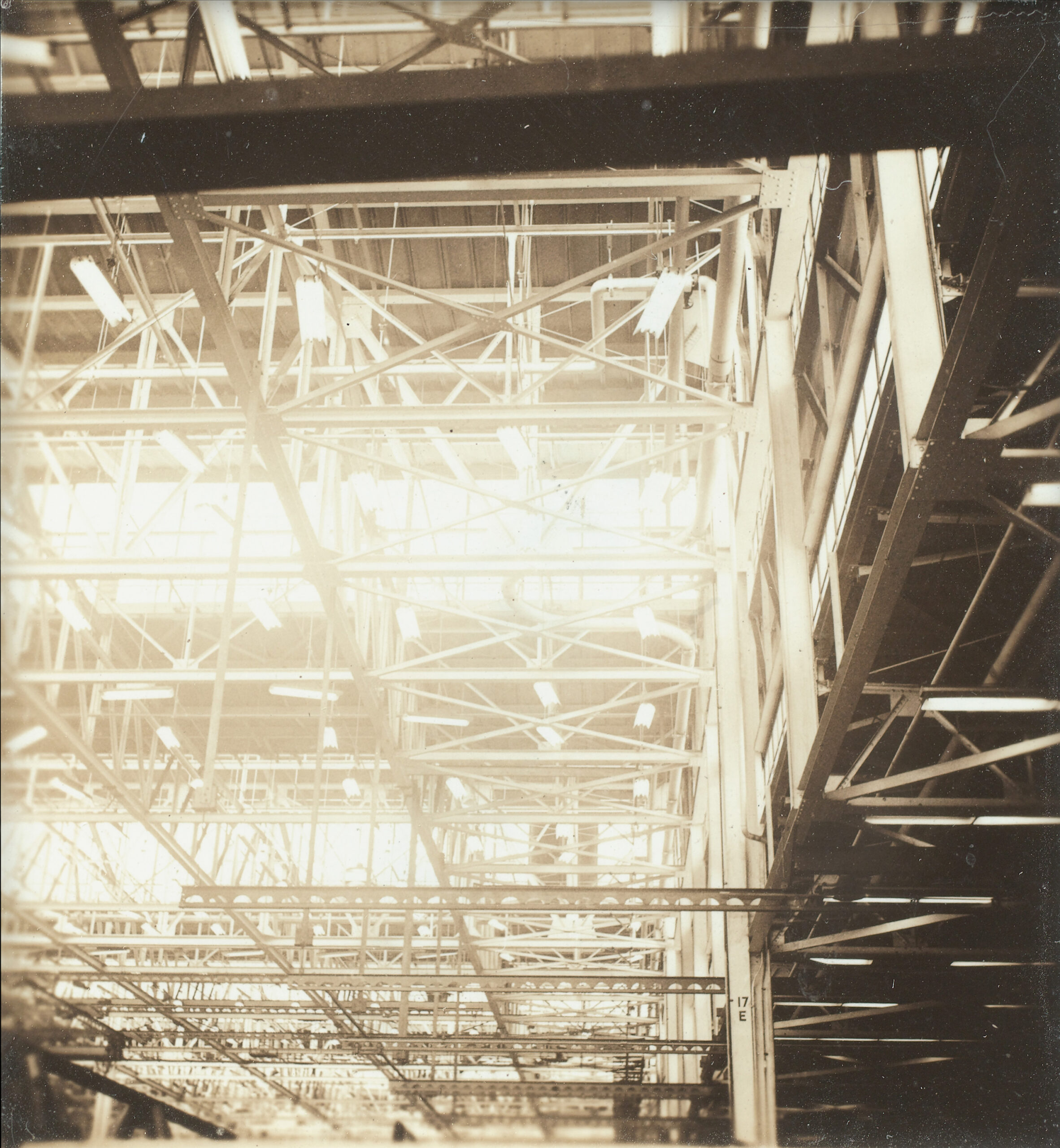 Black and white photograph of rows of light fixtures on the ceiling of an aircraft factory.