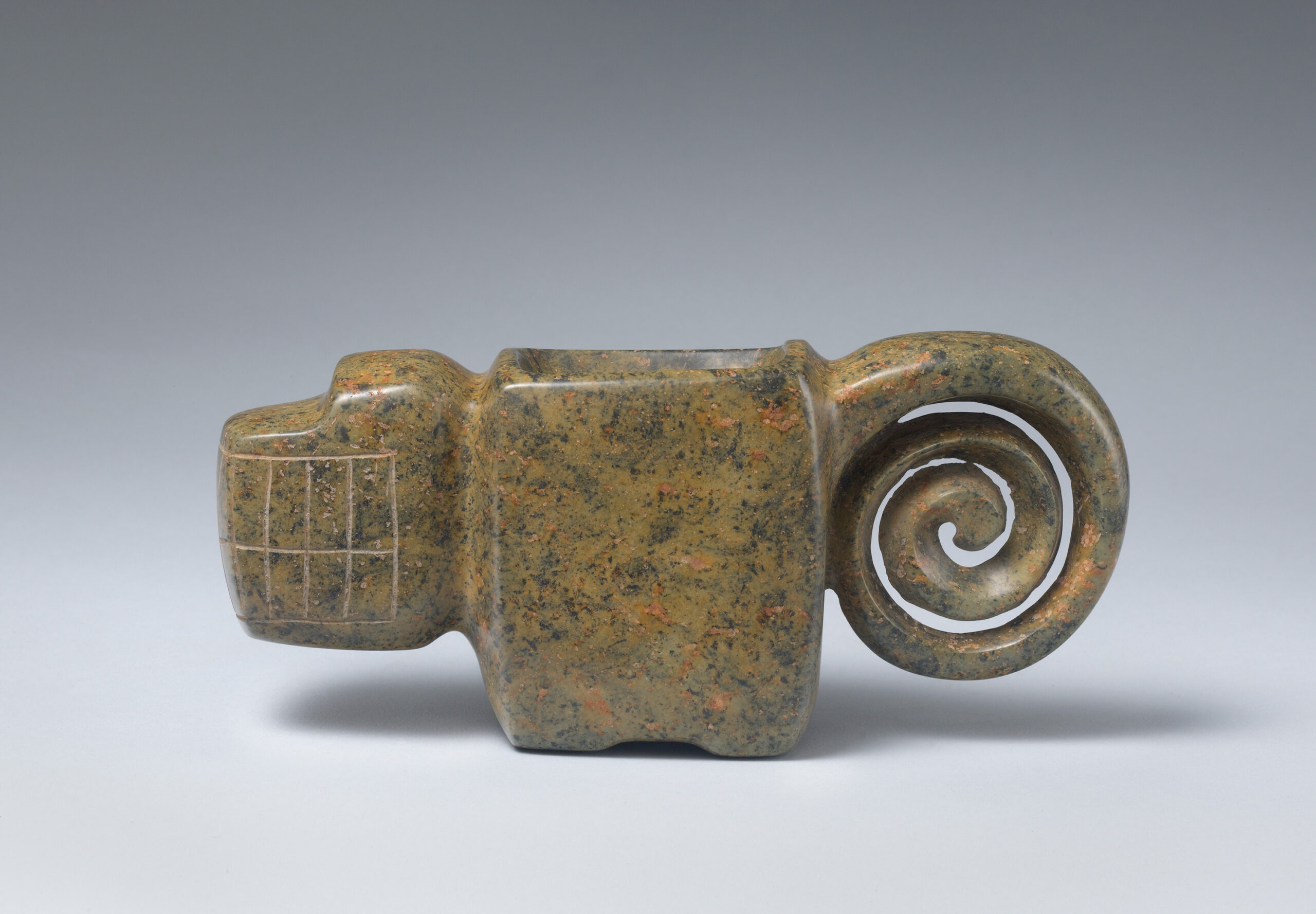 A vessel carved in the abstract shape of a jaguar with an intricate spiral tail.