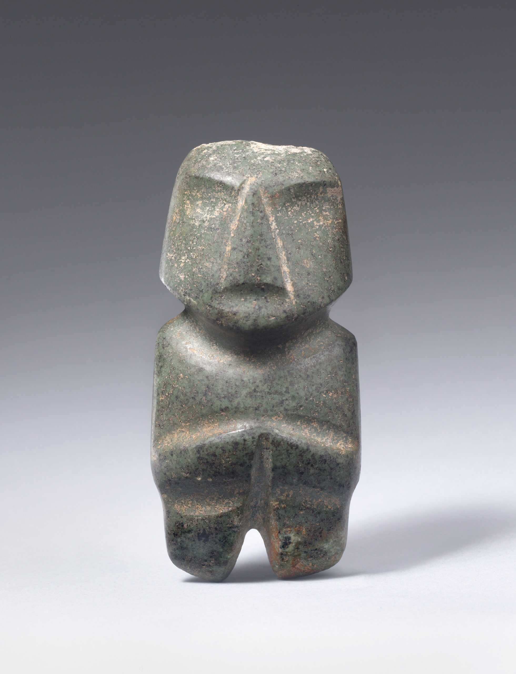 Stone sculpture of an abstracted standing figure with carved facial features and arms at the torso.