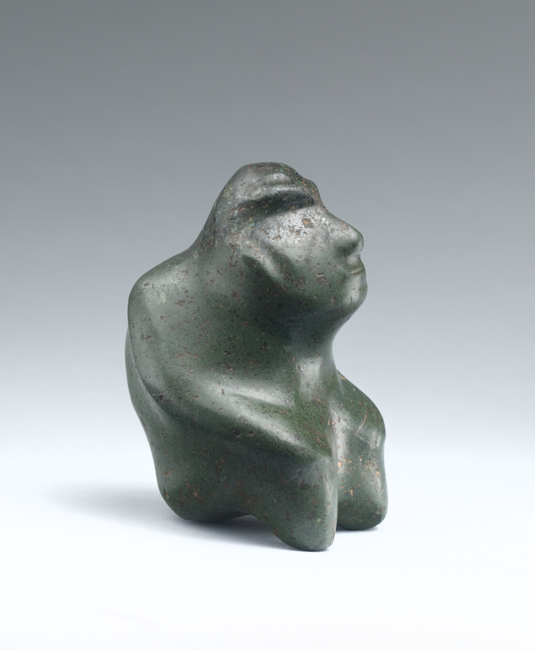 Abstract seated stone figure with a hunched back, naturalistic facial features, and arms resting on the knees.