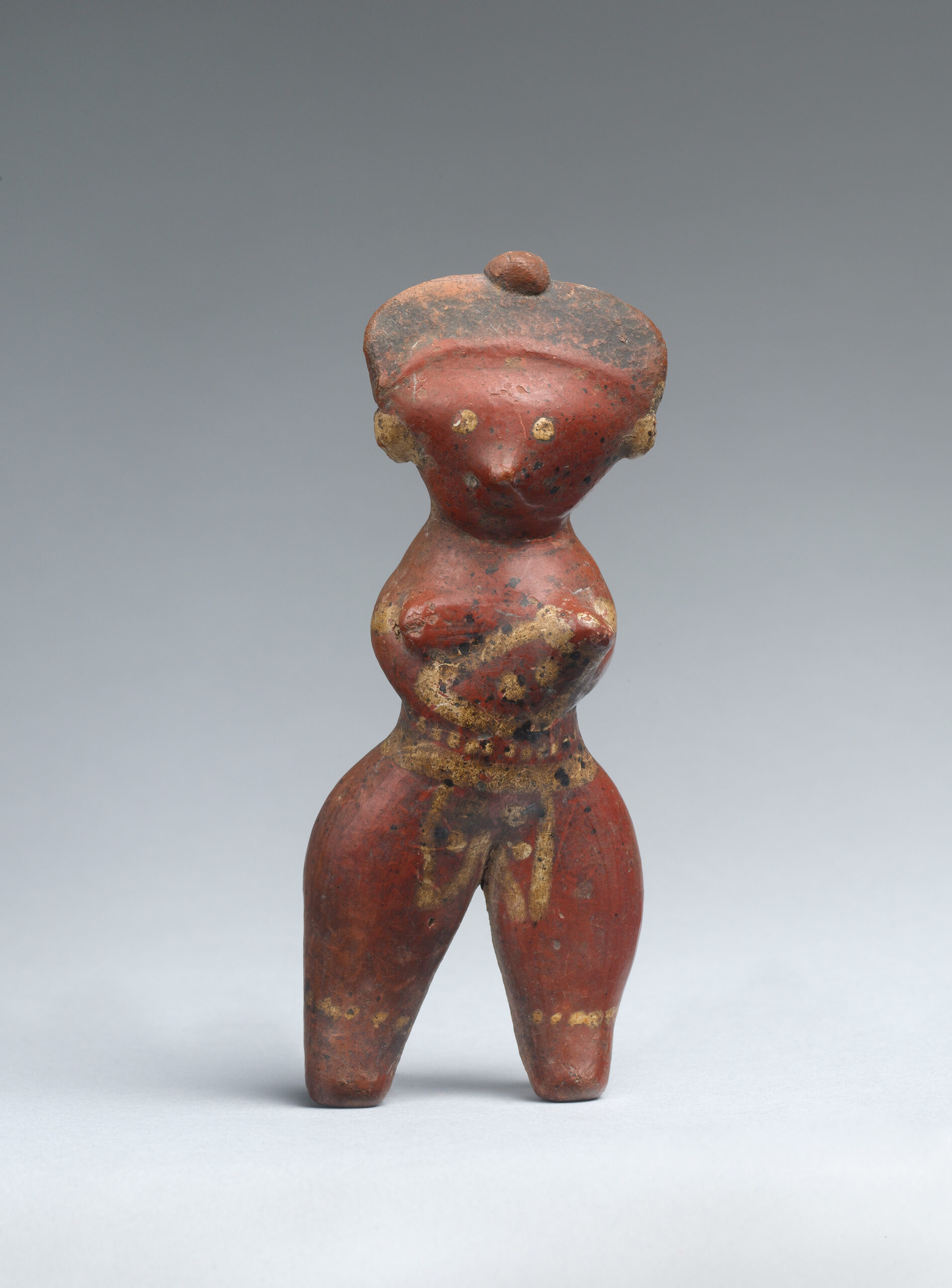 A stylized ceramic standing female figure painted red, yellow, and black.