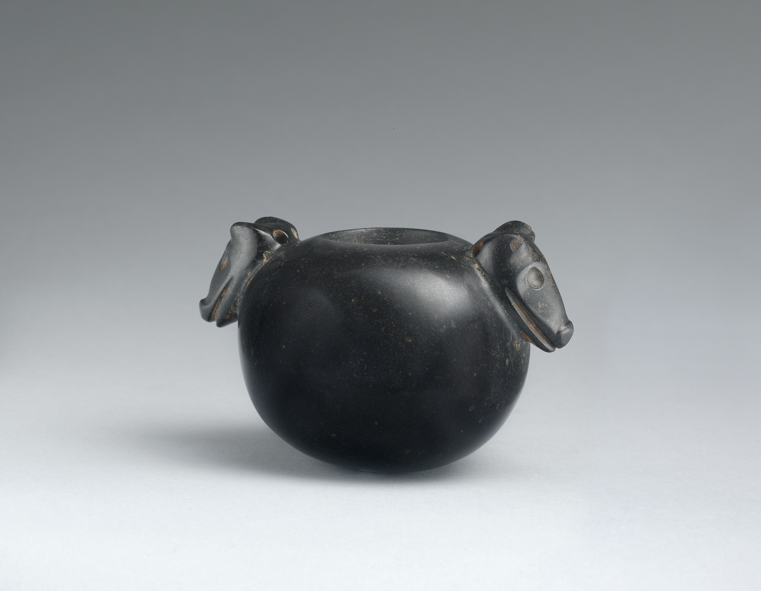 Polished vessel with stylized carving of identical canine heads on each side.