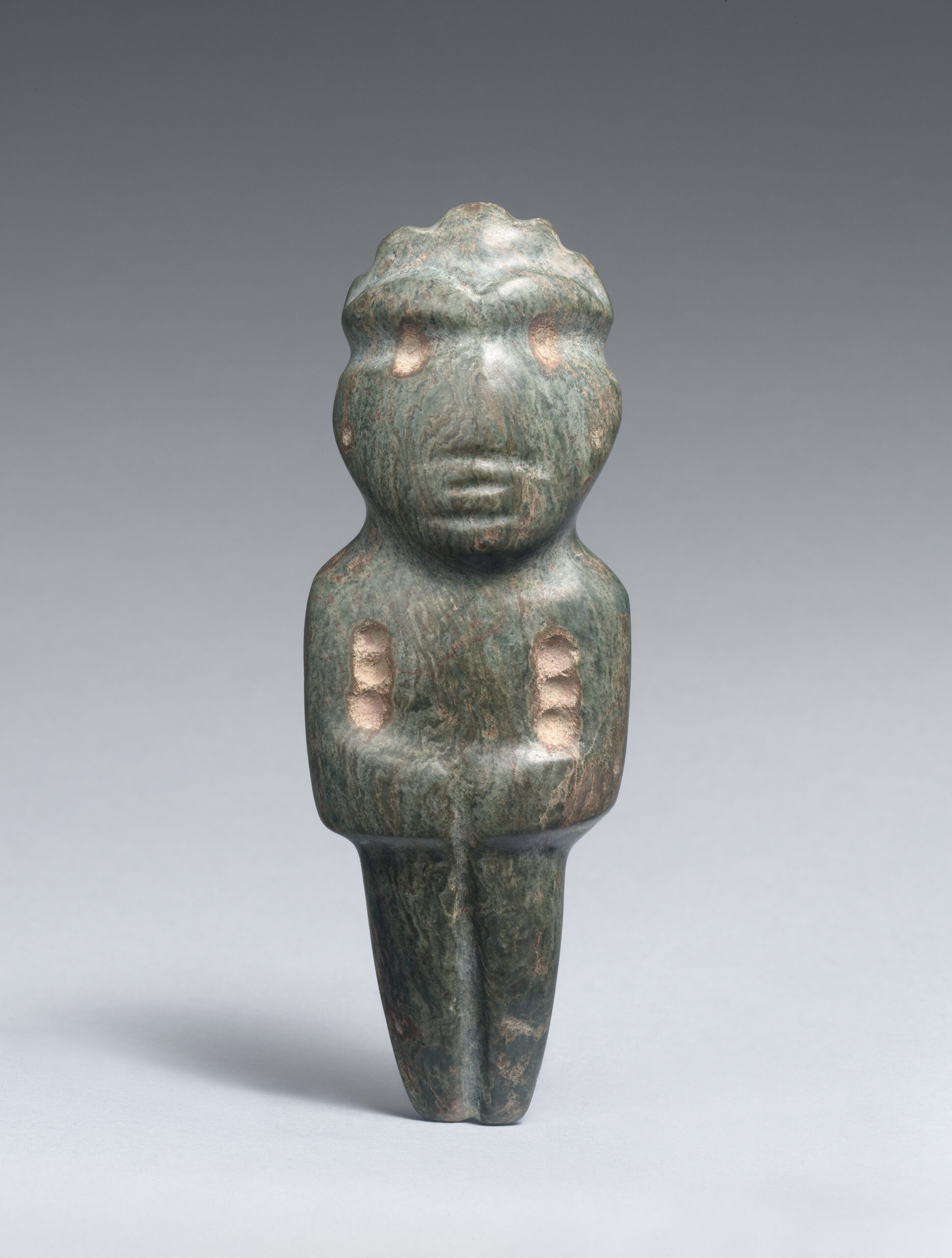 Standing stone figure with pecked round eyes, humanistic facial features, and arms folded across the abdomen.