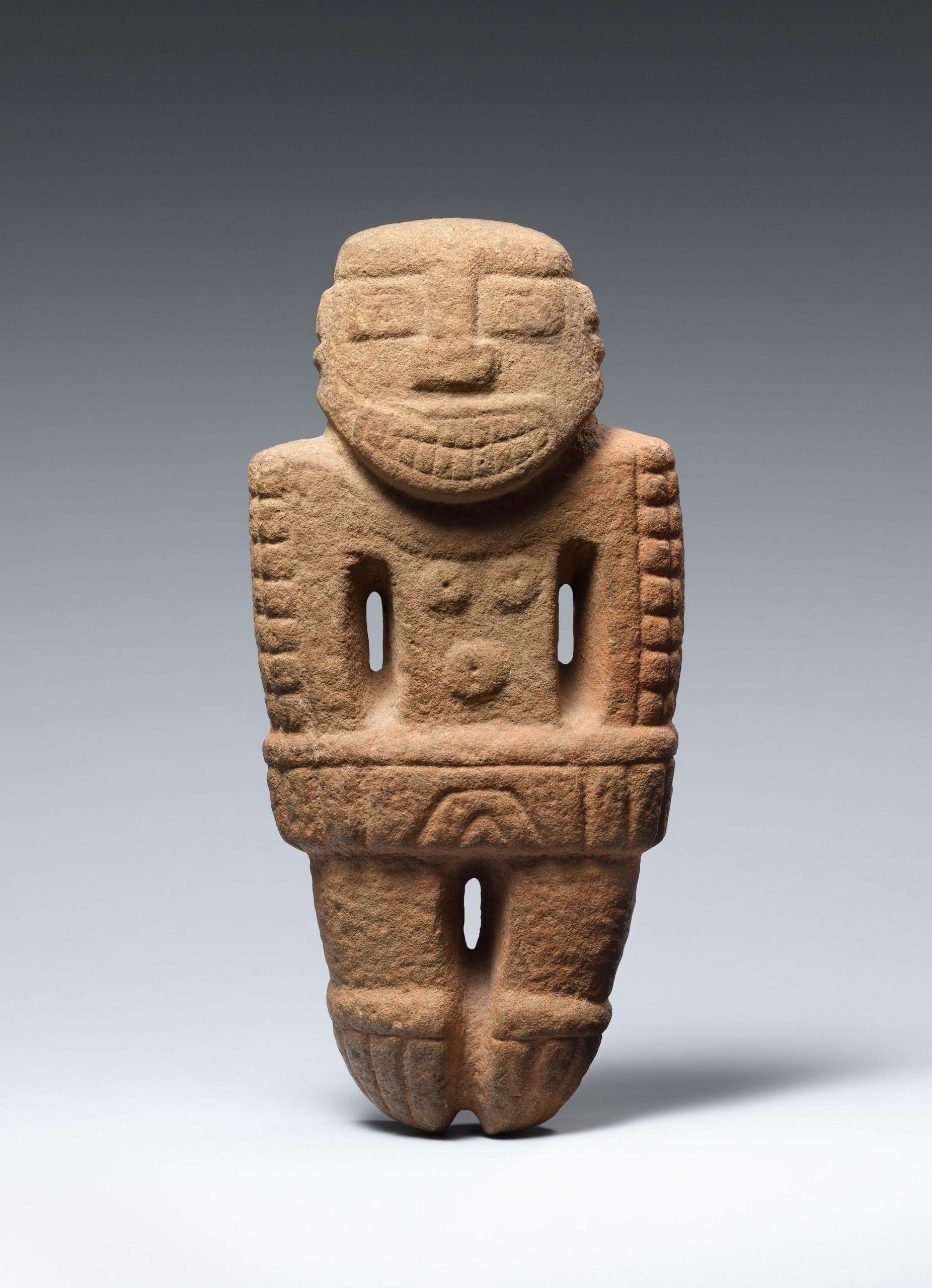 Stone figure wearing a necklace and loincloth, with an open mouth revealing teeth and incised arms at each side.