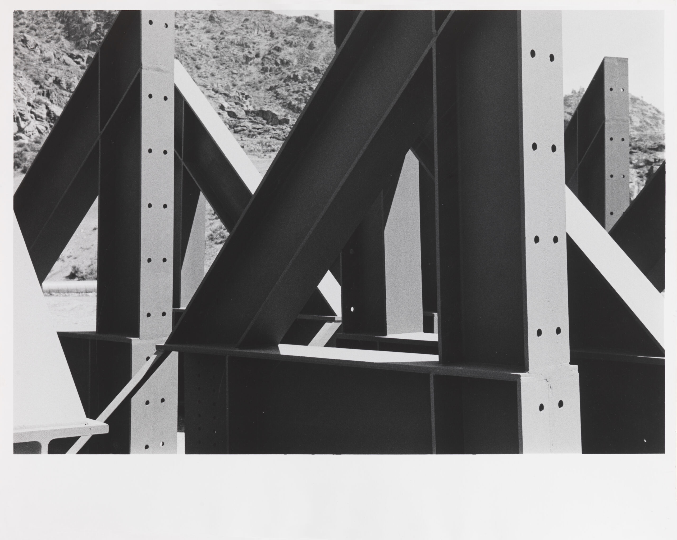 Black and white photograph of girders of the Coulee dam set against rough terrain.