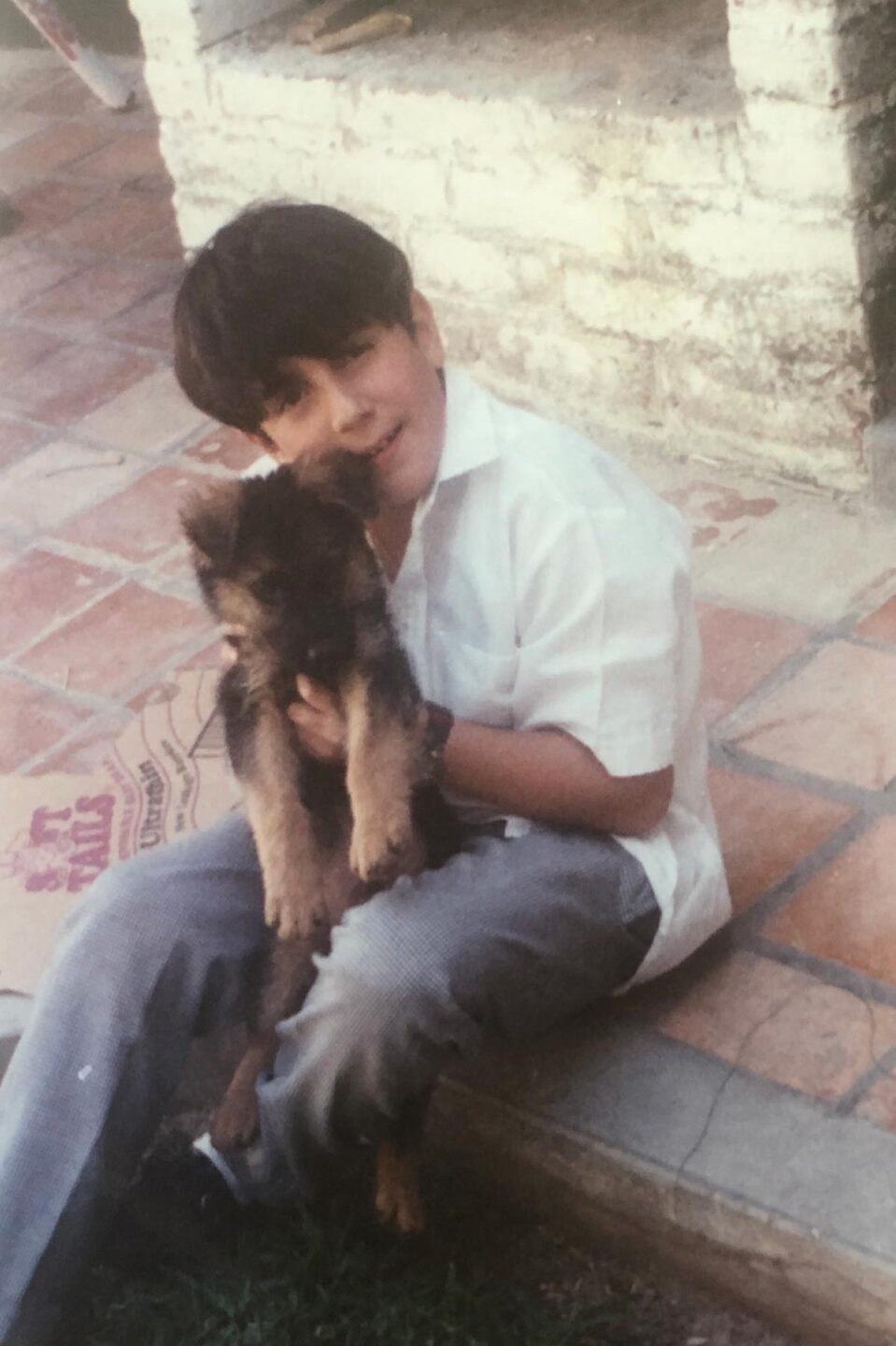 Juan Pablo González hugs a puppy outside on a patio.