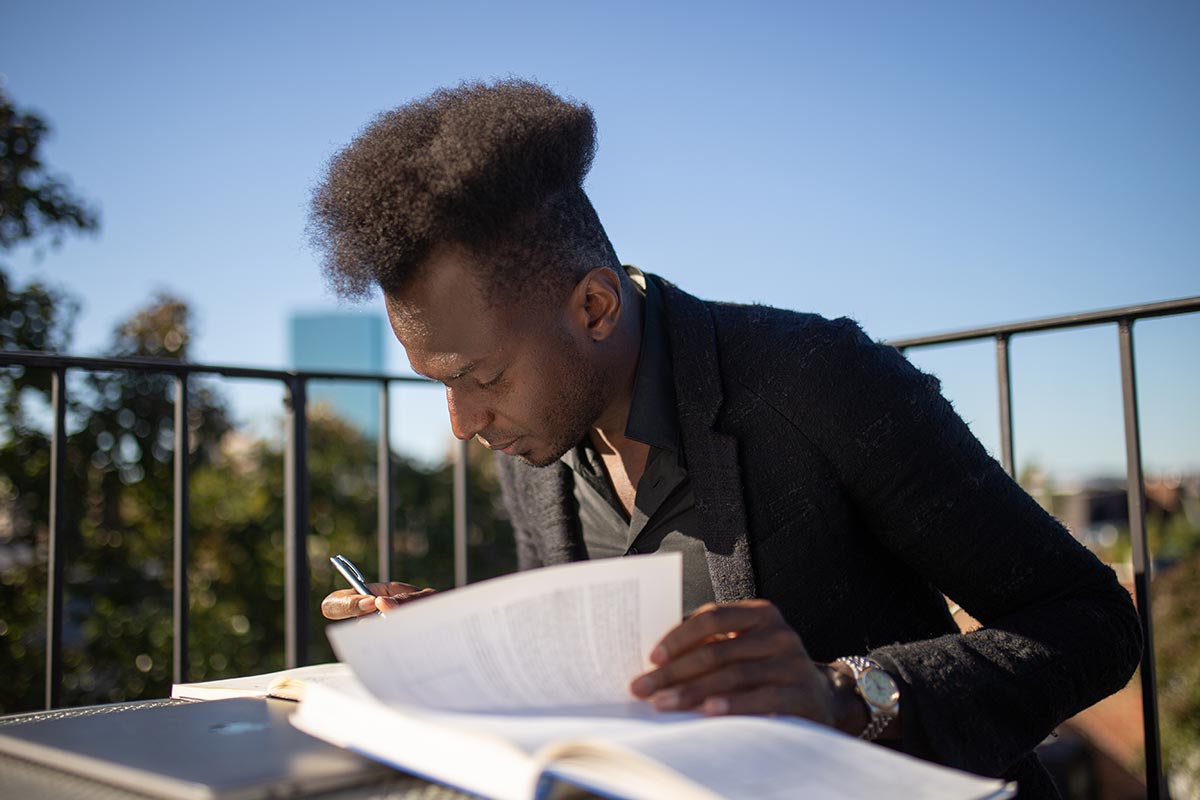 Ibrahim writes in a notebook at a table on a rooftop deck.