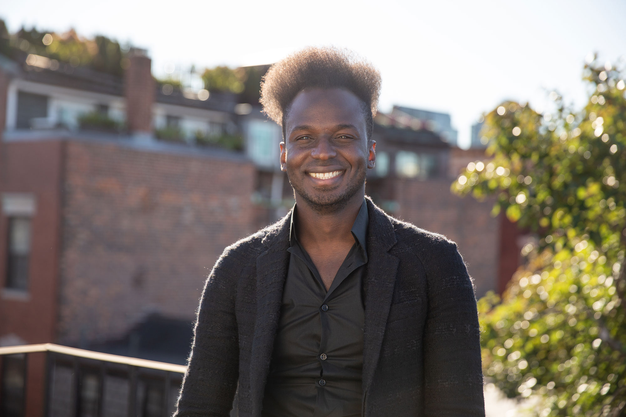 Ibrahim Cissé wearing a black blazer and shirt, smiles standing on a rooftop.
