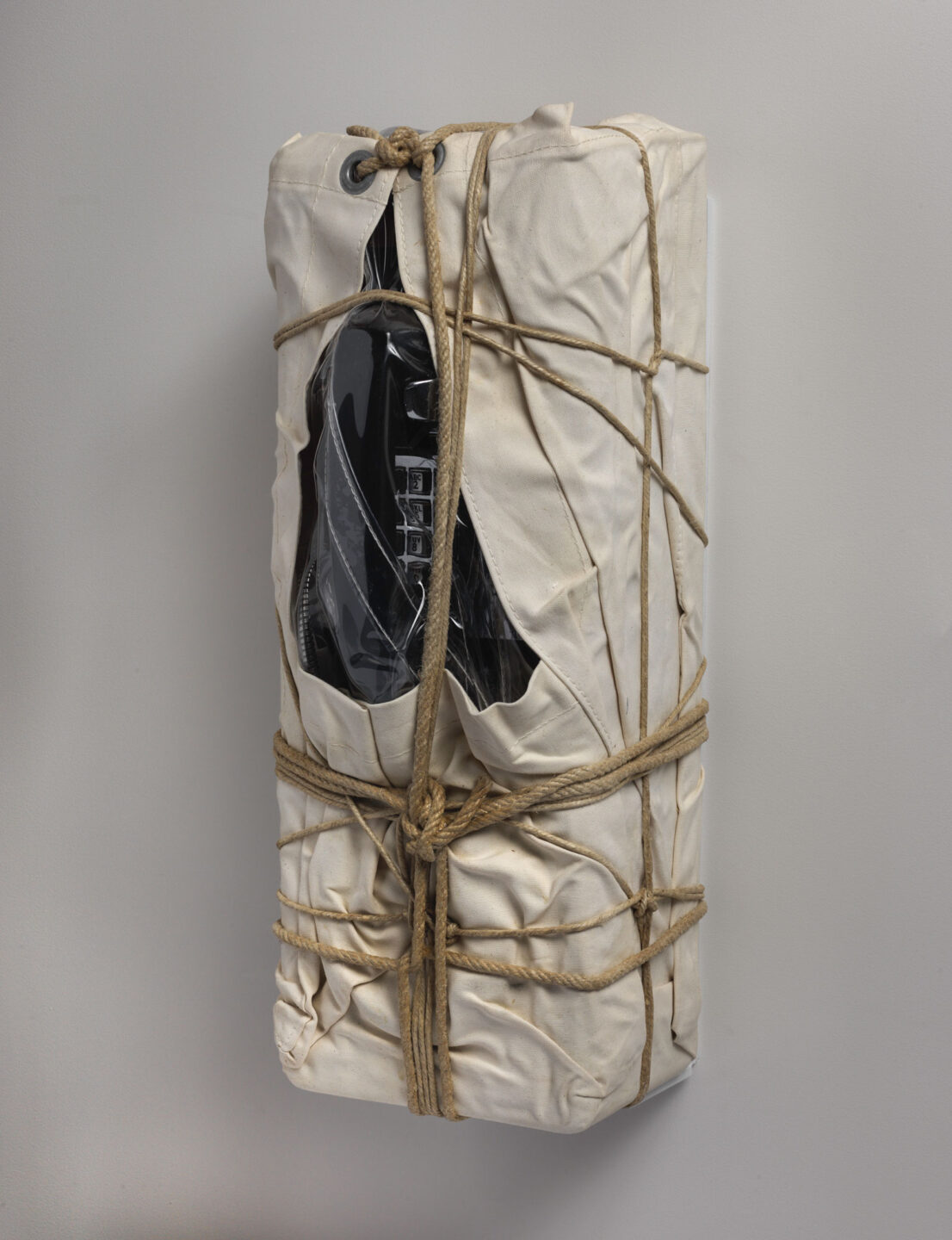 An alternate side view of a payphone wrapped in sackcloth with rope and twine.