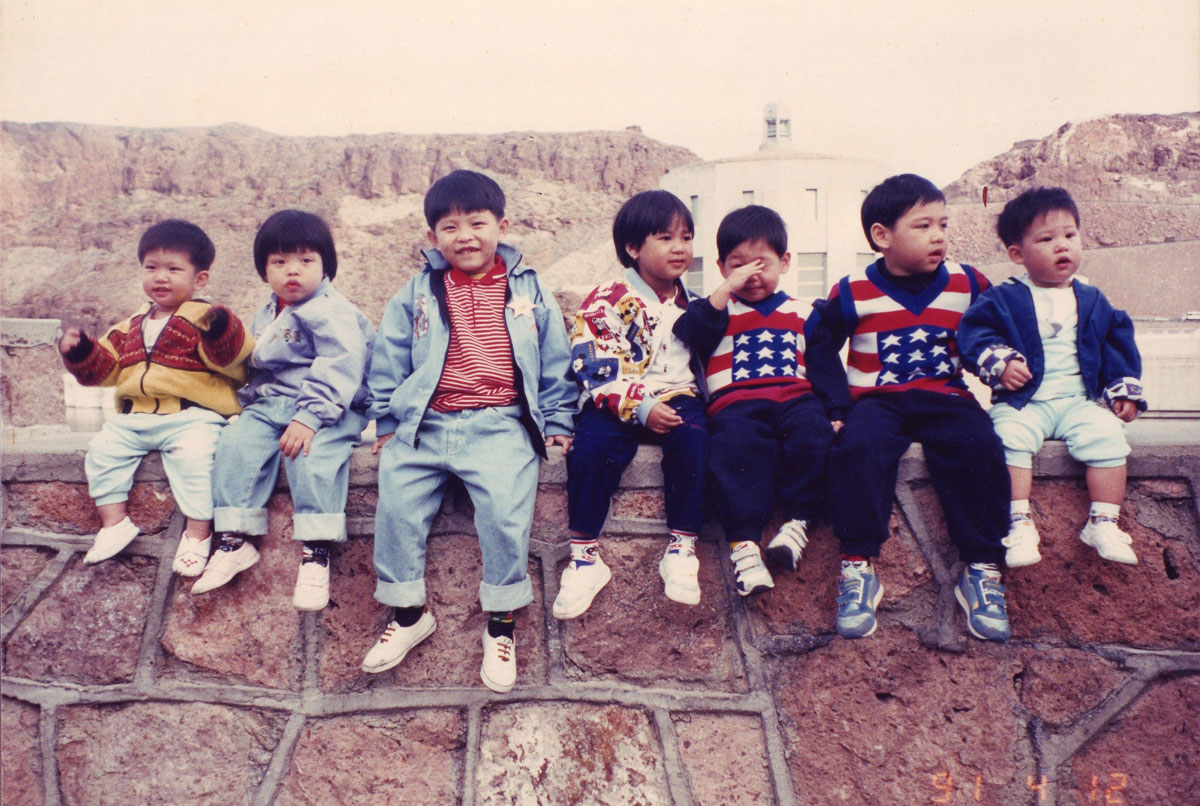 Jirayut “New” Latthivongskorn as a baby alongside family and friends sitting on a wall.