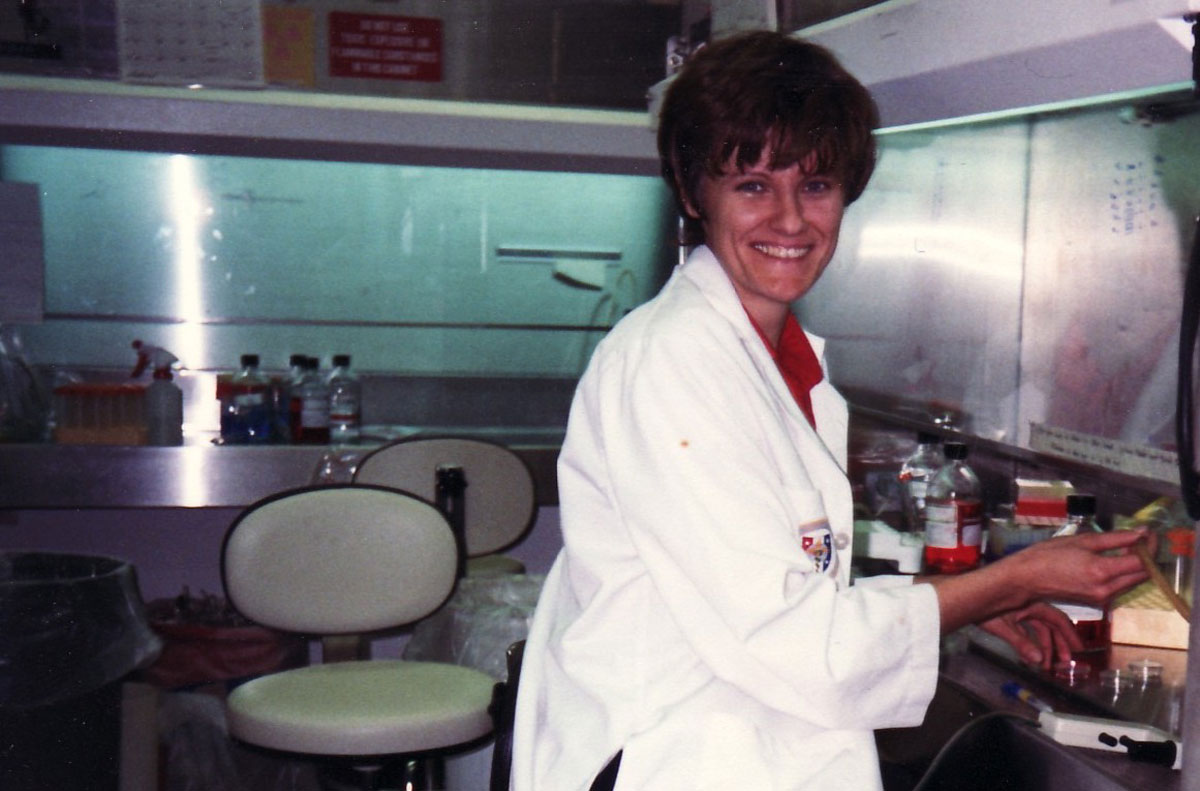 A young Katalin Karikó in a white lab coat working in the lab.