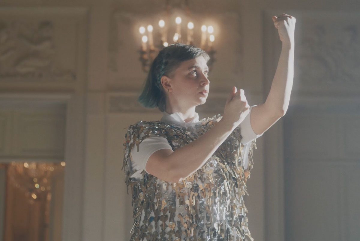 Alice Gosti with her arms raised in fists in front of a chandelier.
