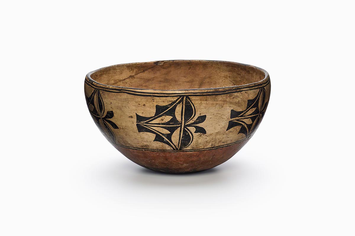 A beige and rust-brown ceramic Cochiti dough bowl with a black emblematic design.