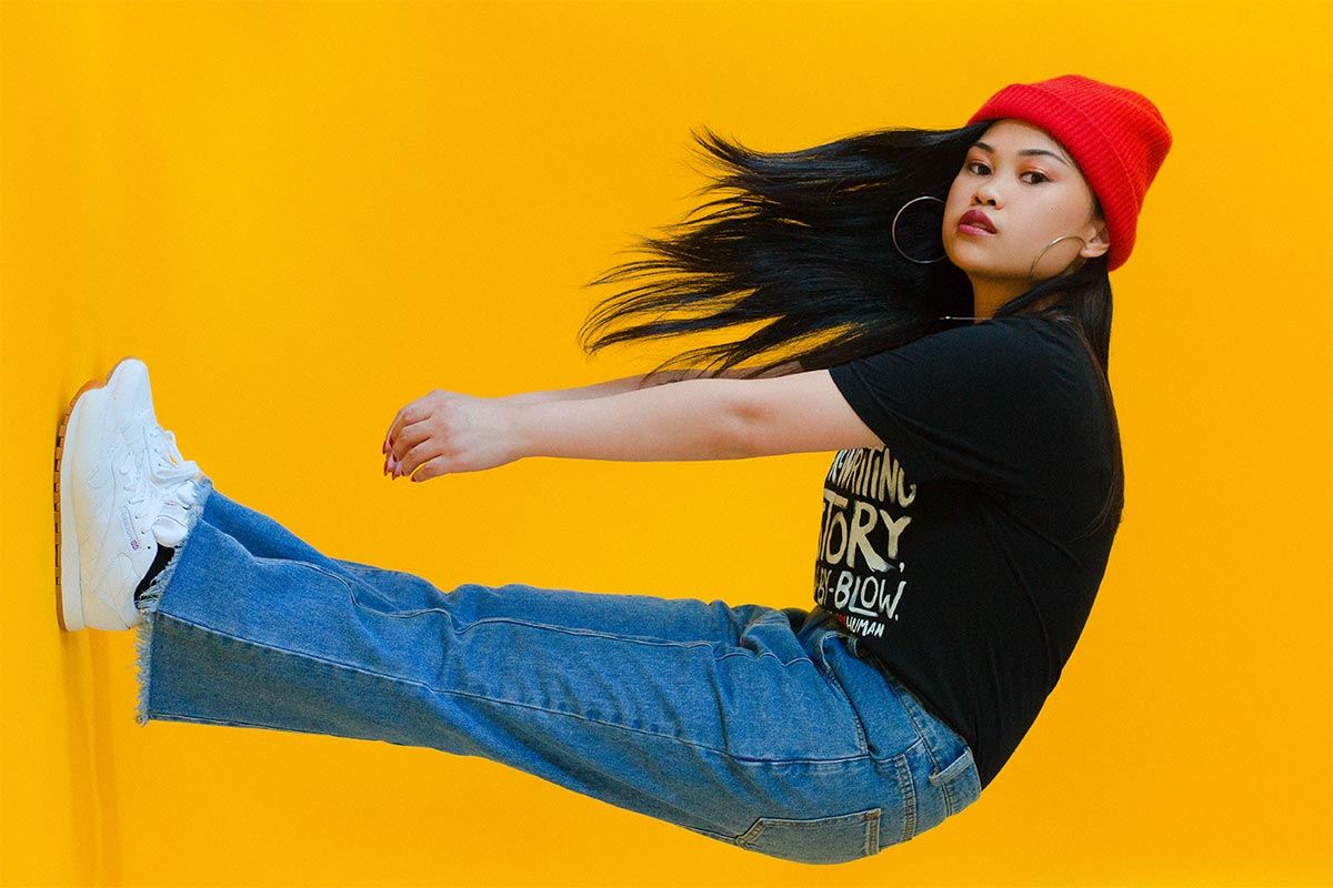 Ruby Ibarra bends while wearing jeans and a red hat.