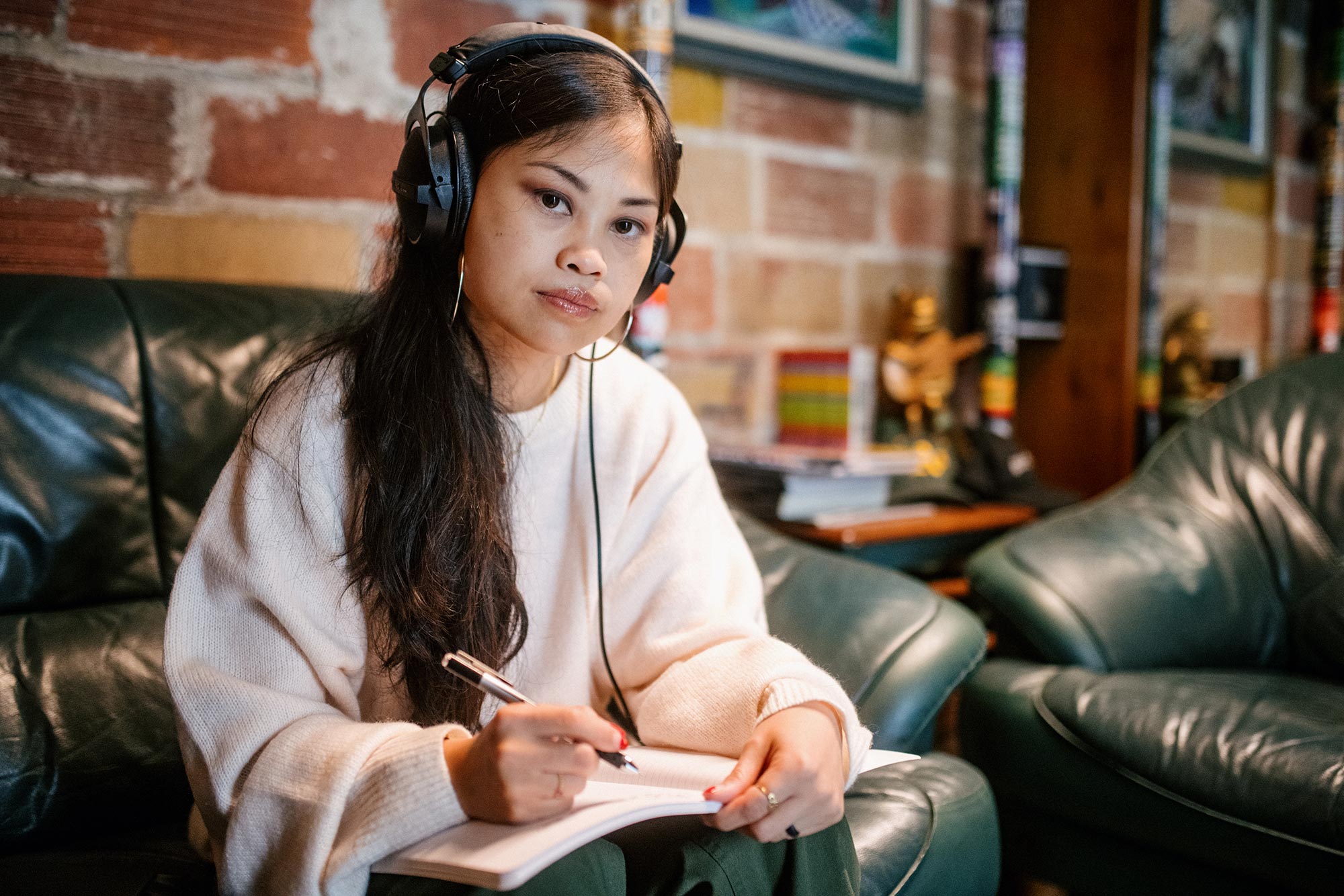 Ruby Ibarra, sitting on a couch with headphones on, writing lyrics in a notebook.