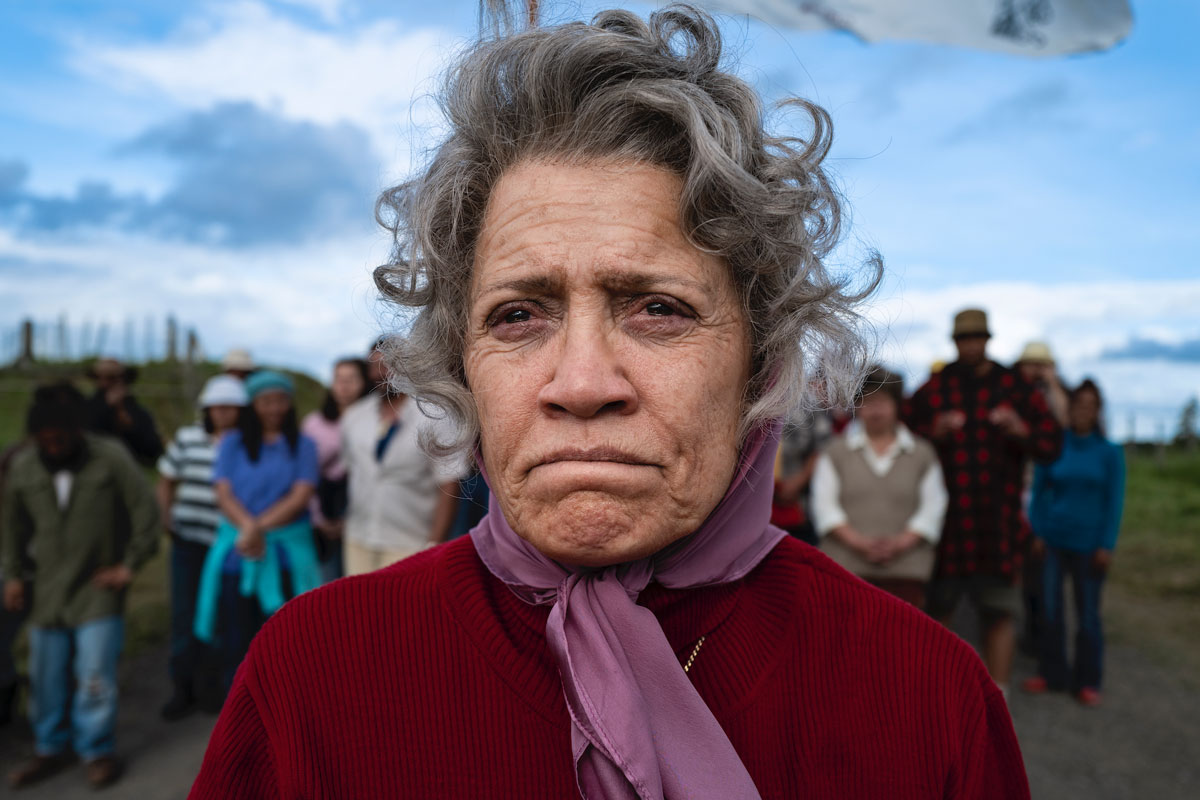 A still from Rena Owen's "Whina": An older women stands outside in front of a group of people.