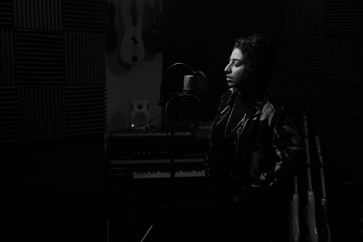 A black and white image of Arooj Aftab singing into a recording microphone.